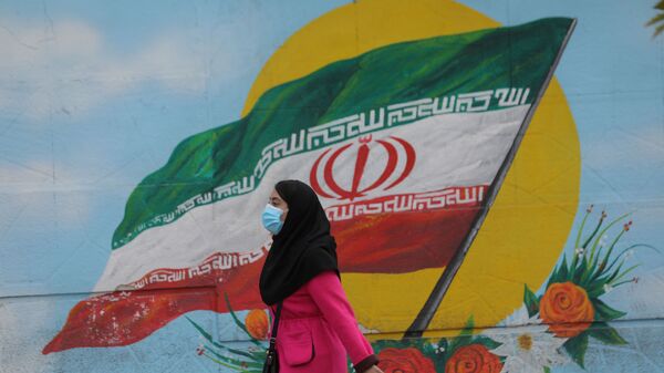 Tahran'da İran bayraklı duvar resminin önünden geçen maskeli kadın - Sputnik Türkiye
