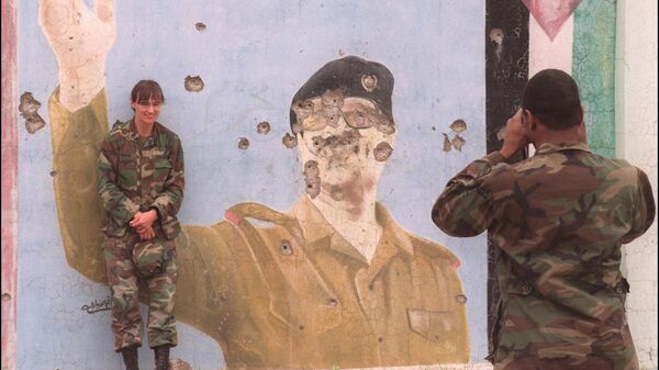 01 Mayıs 1991'de  bir ABD askeri,  meslektaşının Irak Devlet Başkanı Saddam Hüseyin'in kurşunlanmış devasa bir grafiti portresinin önünde poz verirken fotoğrafını çekiyor  - Sputnik Türkiye