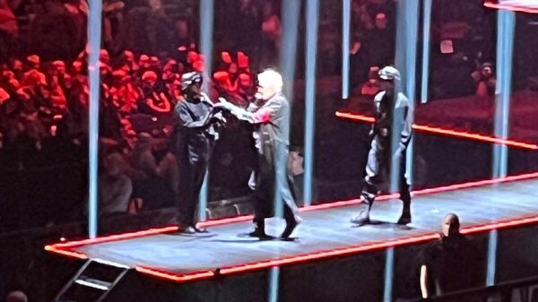 Roger Waters'ın Berlin konserinde siyah deri eldivenler eşliğinde kırmızı kol bandı takılı uzun, siyah deri ceket giydiği, kalabalığa doğru sembolik silah ateşlediği sahne - Sputnik Türkiye