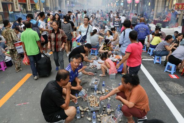 Dandong'un Zhongjin sokağında popüler yerli yemek olan deniztarağı pişirip yerken insanlar. - Sputnik Türkiye