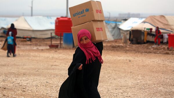 Suriyeli kadın sığınmacı Deyr Ez Zor'dan kaçmış Haseke'deki kampta UNICEF yardım kutularını taşıyor - Sputnik Türkiye